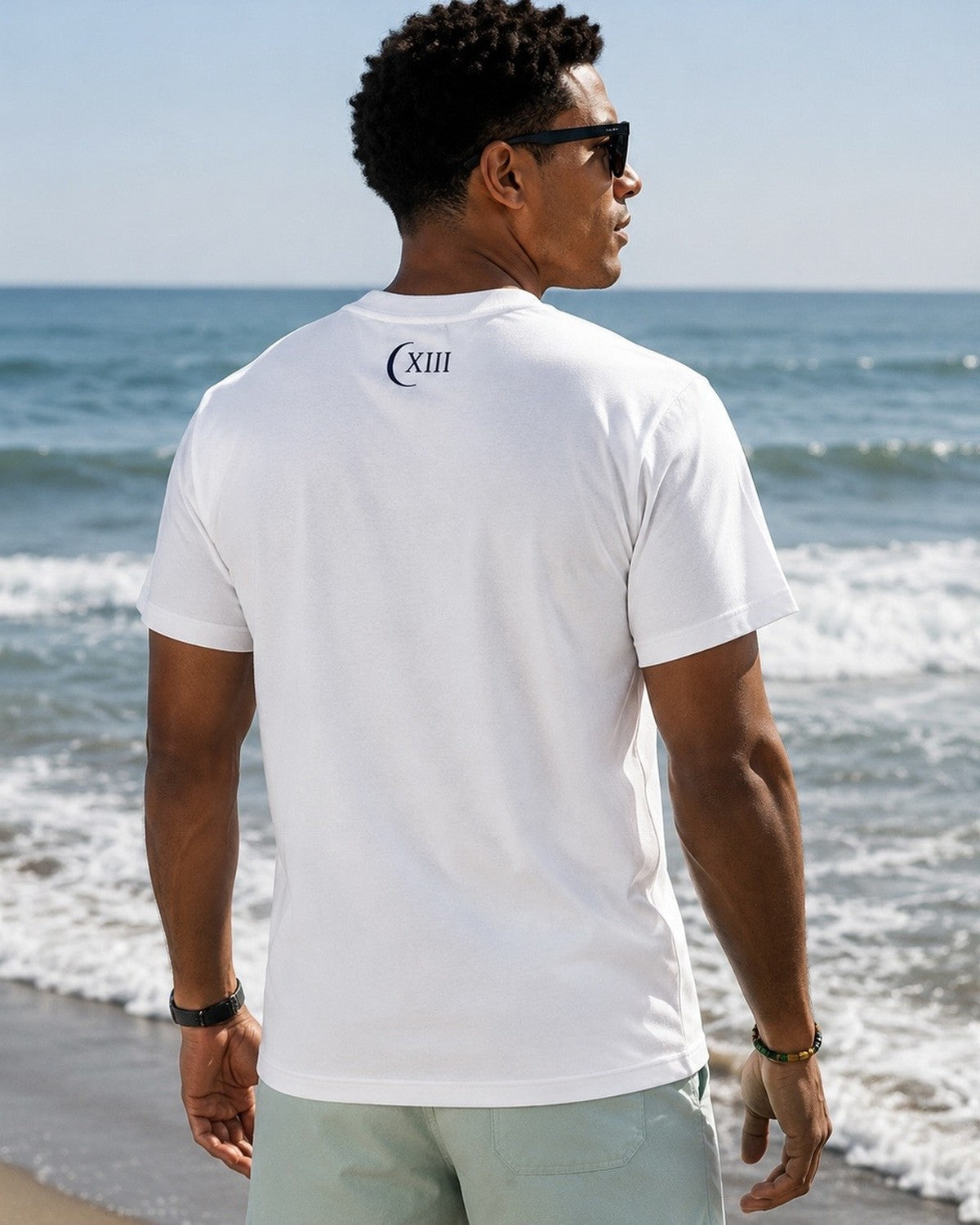 Camiseta Atlantic Pure — modelo de espaldas frente al mar, luna y numeral XIII en la nuca