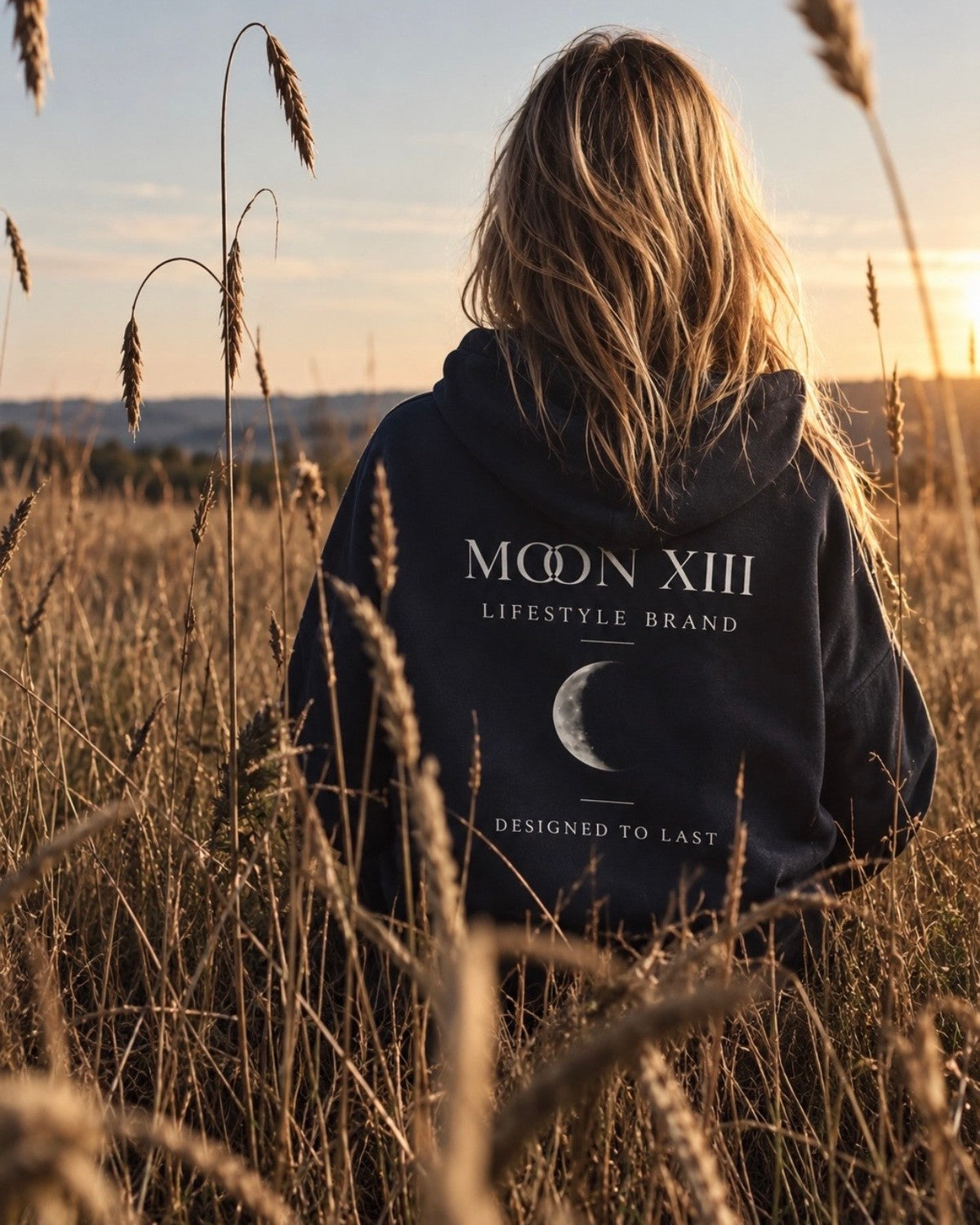Sudadera con capucha Heritage Navy — modelo de espaldas en un campo de trigo al atardecer