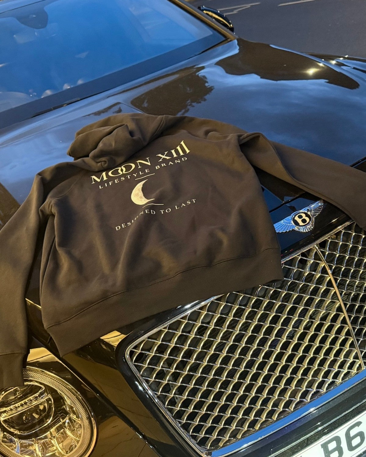 Sudadera con capucha Heritage Navy — de espaldas sobre el capó de un coche, con el logo Moon XIII