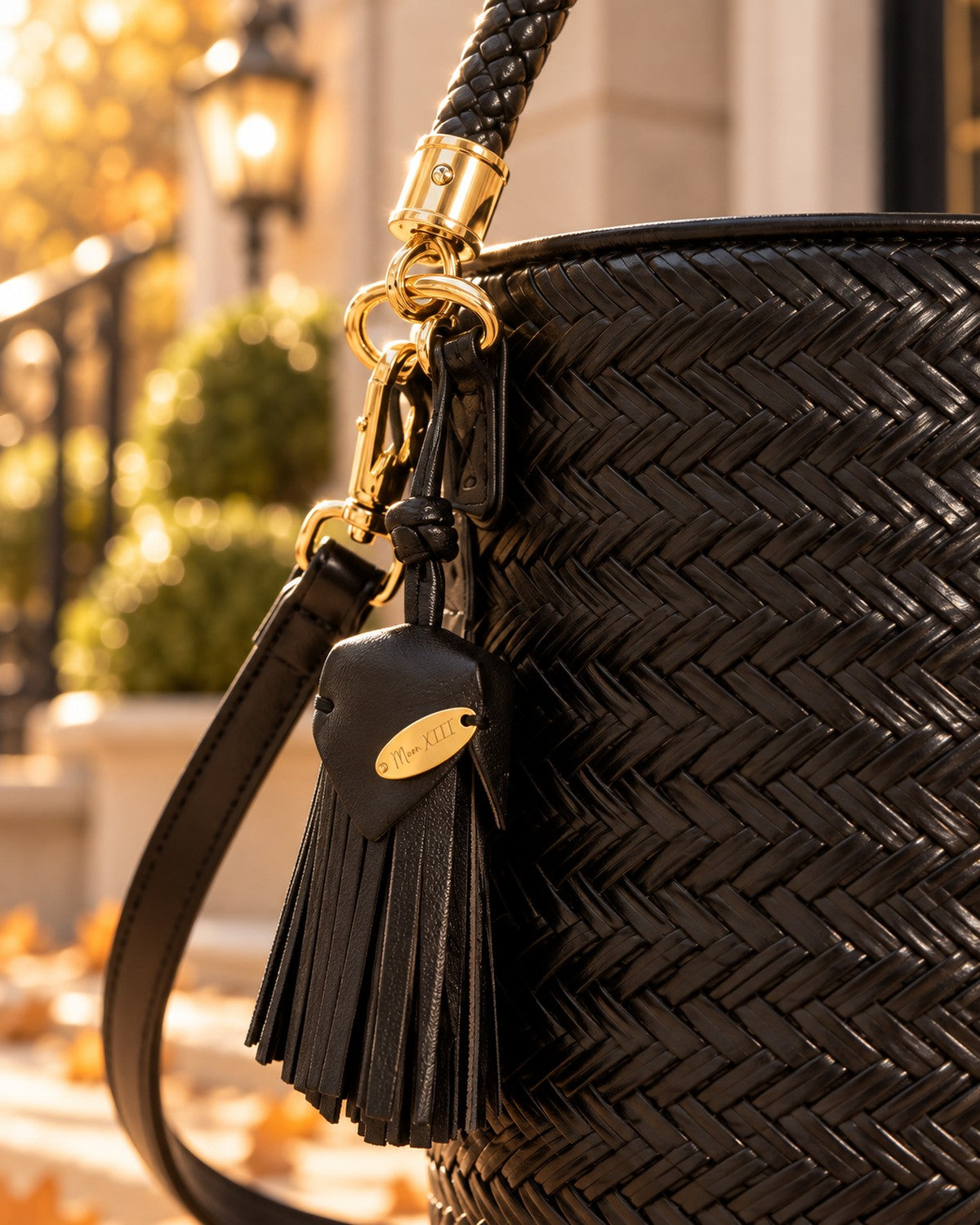 Bolso Capri Noir — detalle de la borla con placa dorada y el mosquetón, a la luz de otoño